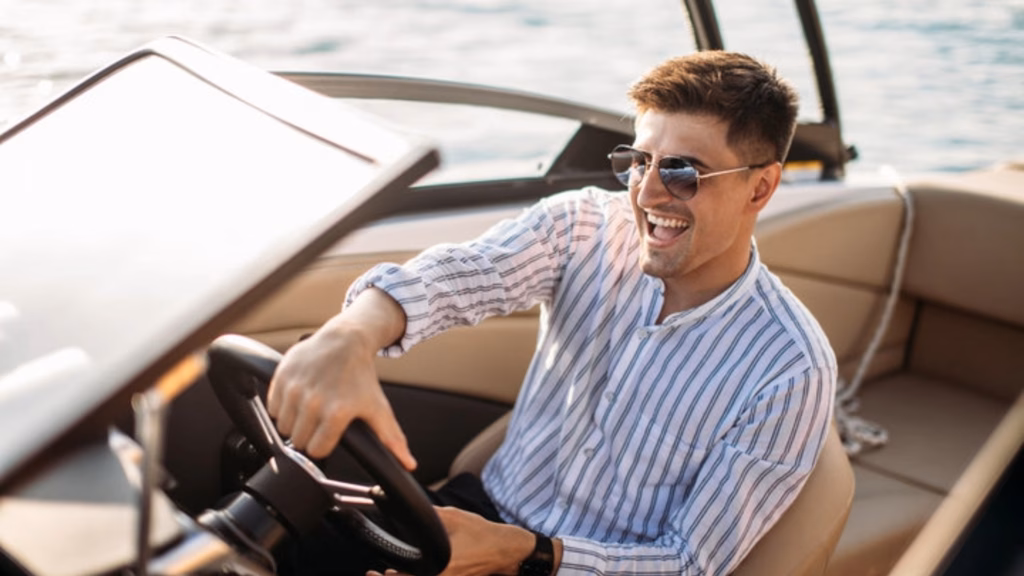 A man wearing sunglasses and a striped shirt driving a boat on the water