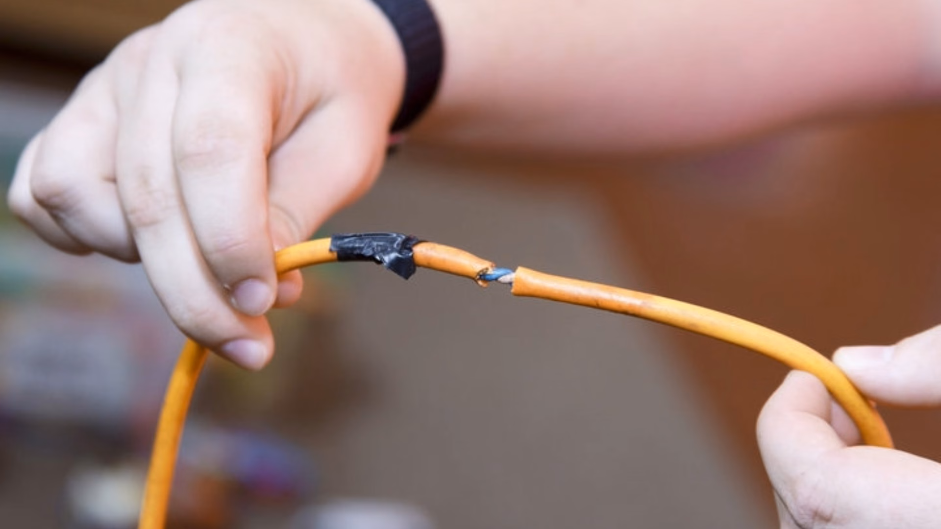 Hands holding a damaged and frayed orange electrical wire